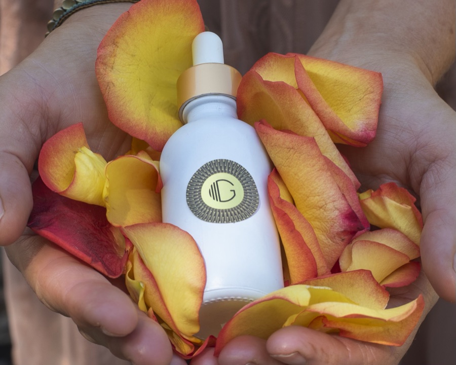 Hands cradling a bottle of Kissed by G among rose petals